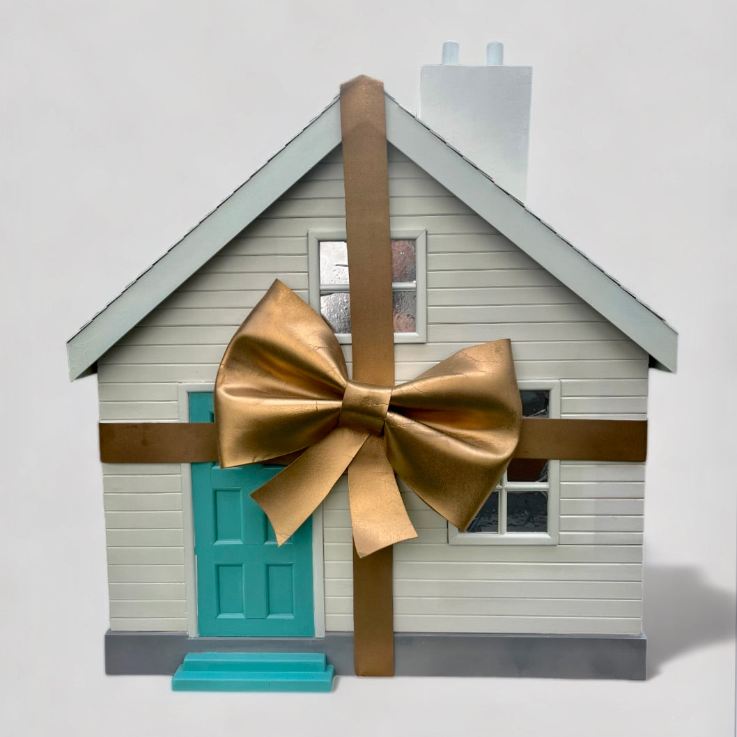 A white wooden house with large gold bow and turquoise front door from Fortnums