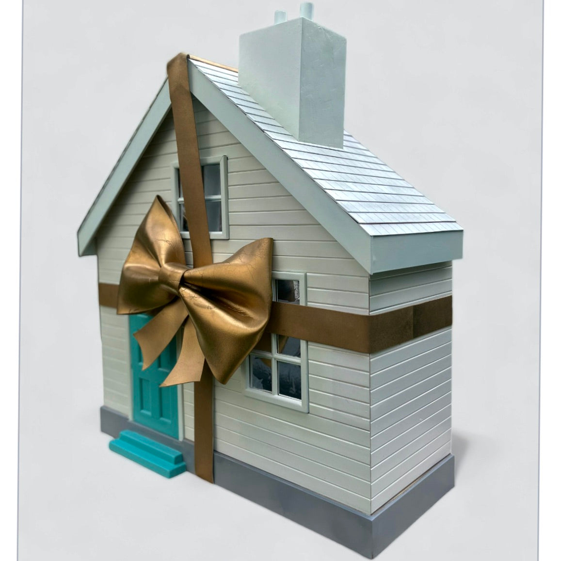 A white wooden house with large gold bow and turquoise front door from Fortnums windows