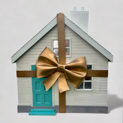A white wooden house with large gold bow and turquoise front door from Fortnums