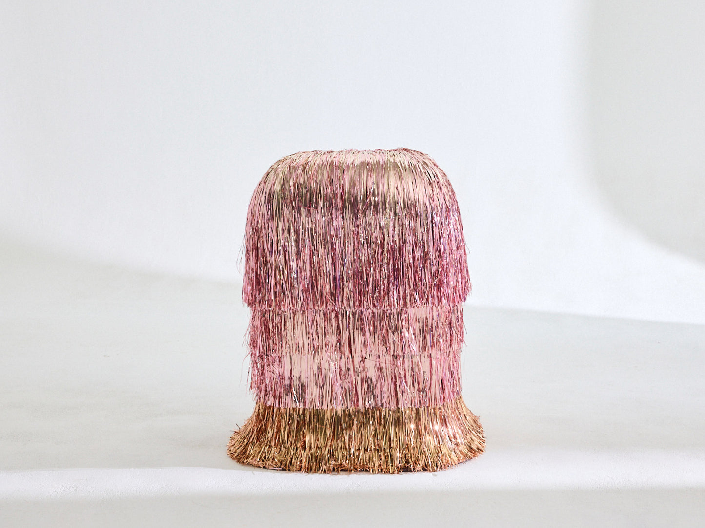 A pink side table covered in three layers of pink tinsel with a bottom layer of gold tinserl 
