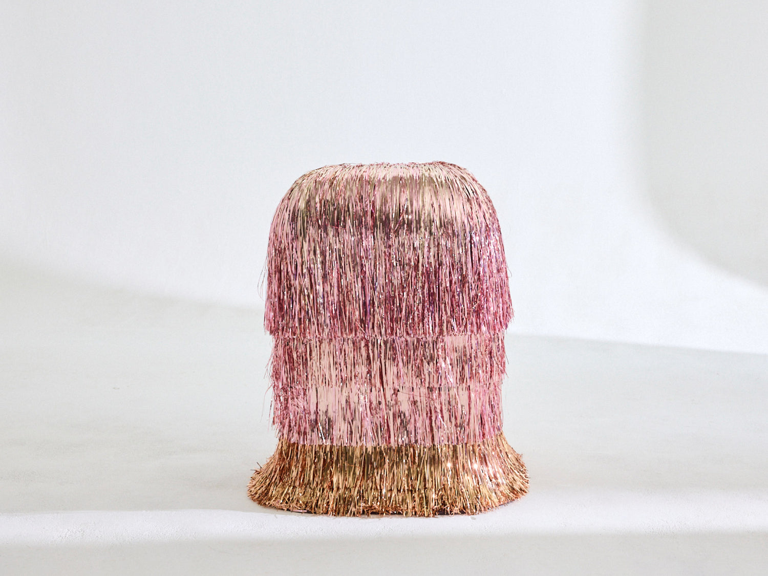 A pink side table covered in three layers of pink tinsel with a bottom layer of gold tinserl 