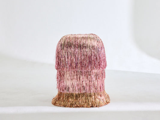 A pink side table covered in three layers of pink tinsel with a bottom layer of gold tinserl 